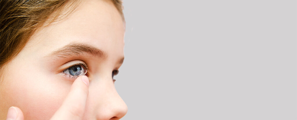 Teen placing contact lens in her eye during contact lens fitting